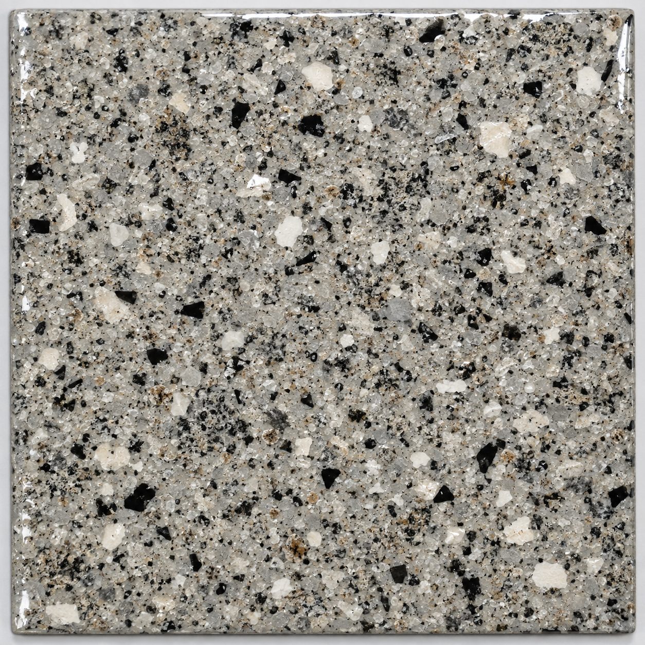 A granite-look broadcast flake concrete floor coating sample in warm gray, cream, and black.